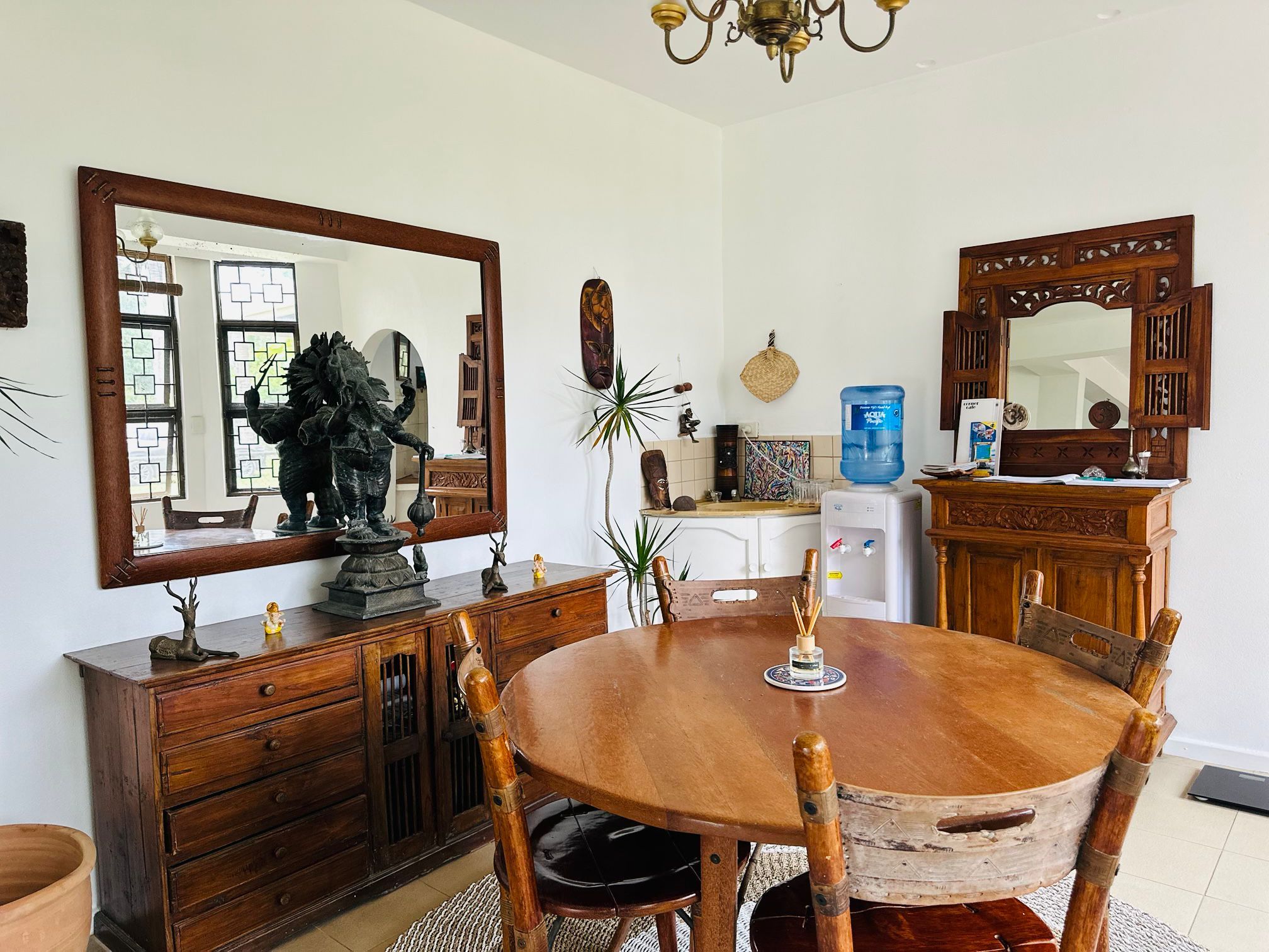 Een eethoek met een ronde houten tafel, stoelen, een grote spiegel en een waterdispenser.