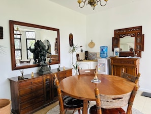Een eethoek met een ronde houten tafel, stoelen, een grote spiegel en een waterdispenser.
