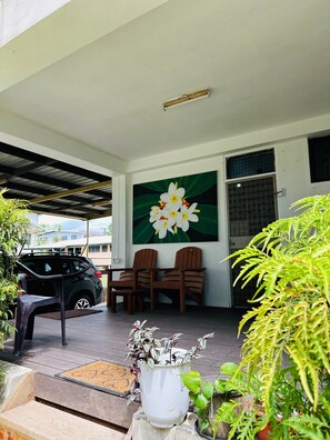 A covered outdoor seating area with a car parked nearby, a large flower painting on the wall, and various potted plants. - Residence 71 (Nadi)