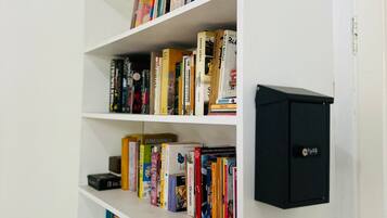 A bookshelf with various books and a black electronic device on the wall.