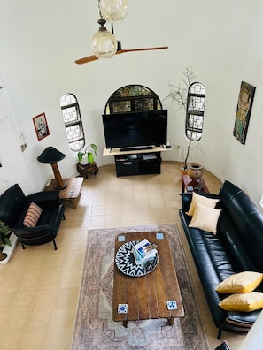 Een woonkamer met een flatscreen televisie, zwarte leren banken, een houten salontafel en een kamerkleed met een patroon.
