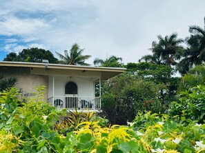 A house with a covered porch, surrounded by lush greenery and palm trees. - Residence 71 (Nadi)