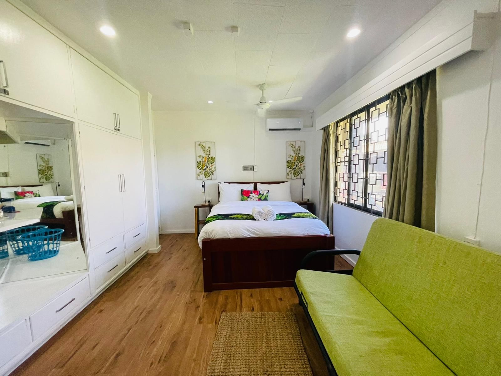A hotel room with a bed, a green sofa, a wardrobe, a desk with a mirror, and a window with curtains.