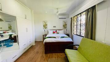 A hotel room with a bed, a green sofa, a wardrobe, a desk with a mirror, and a window with curtains.