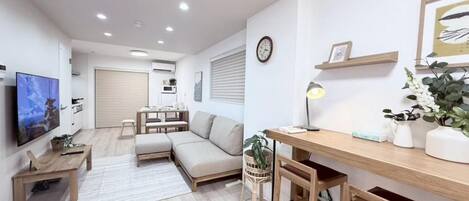 Una sala de estar moderna con un sofá, una mesa de centro de madera, un televisor y un escritorio con una lámpara.