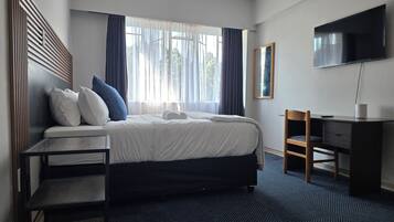 Habitación de hotel con cama, escritorio, silla, televisor y ventana con cortinas.