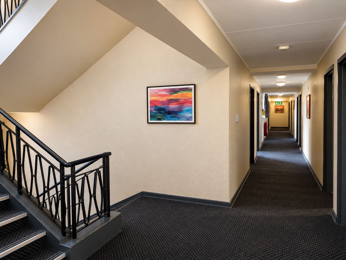 Un couloir d’hôtel avec un escalier, des revêtements de sol en moquette et un tableau encadré accroché au mur.