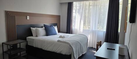 A hotel room with a bed, bedside table, and a desk with a chair.