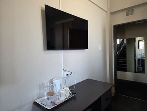A room with a flat-screen TV mounted on the wall, a coffee maker, and a tray with cups and glasses.