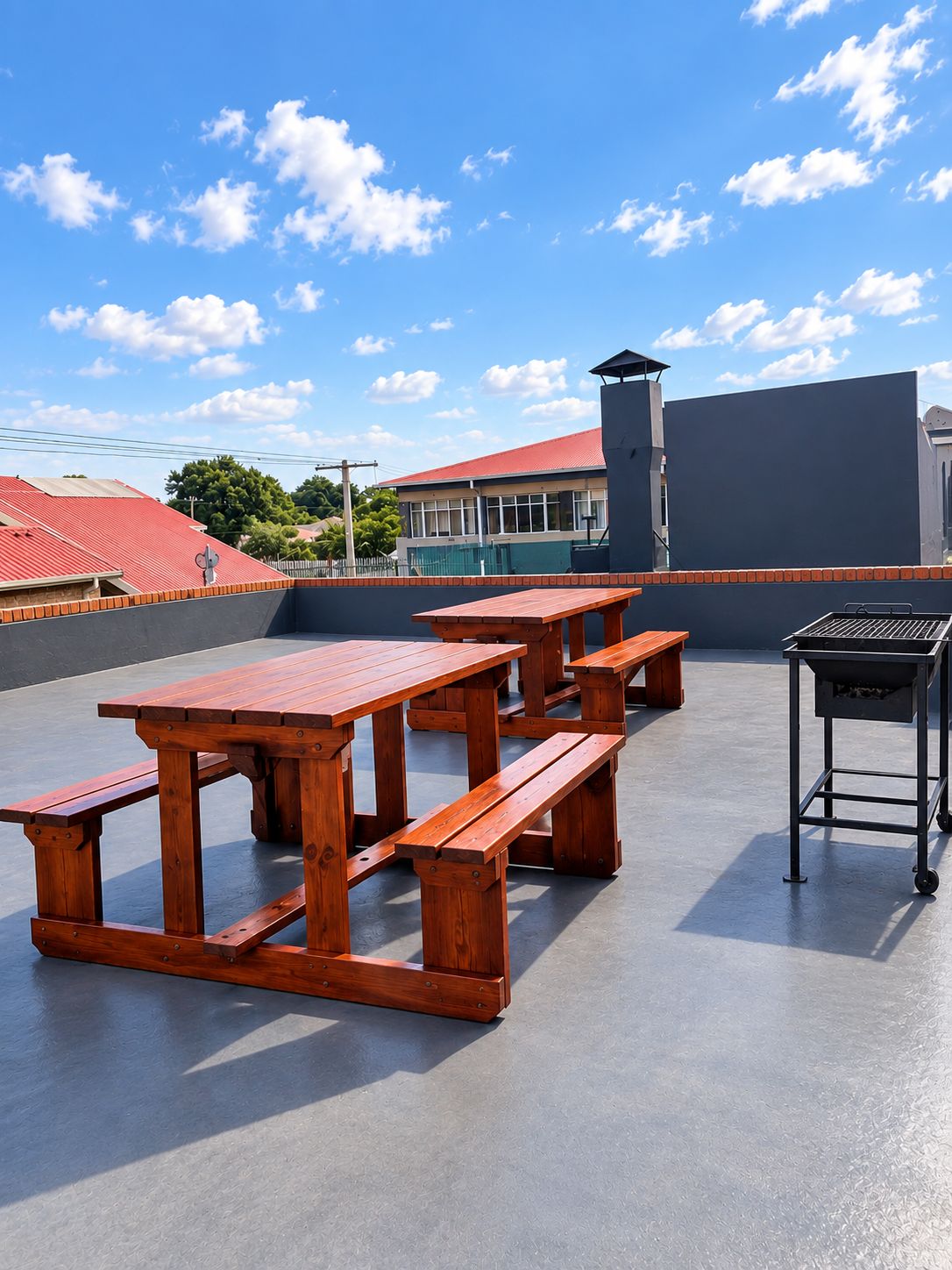 Un patio al aire libre con mesas de picnic de madera y una parrilla.