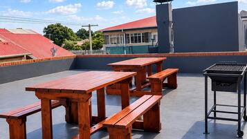 Un patio al aire libre con mesas de picnic de madera y una parrilla.