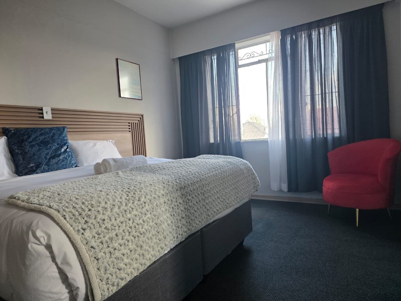 A hotel room with a bed, a red chair, and a window with curtains.