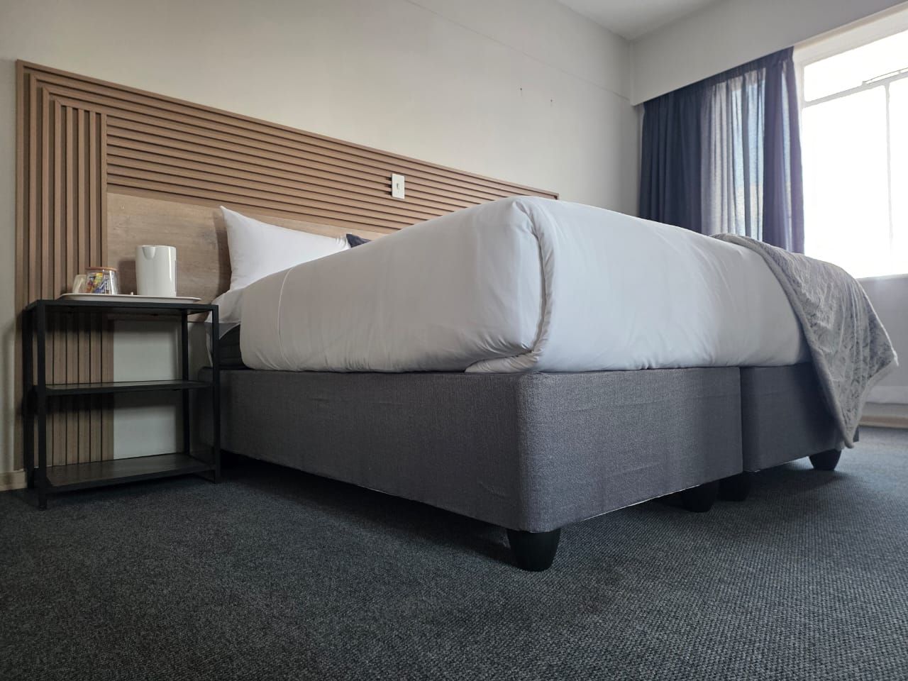 Una habitación de hotel con una cama, una mesita de noche y una ventana con cortinas.