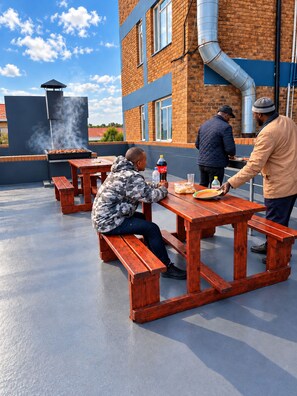 A rooftop patio with wooden benches and a barbecue grill.