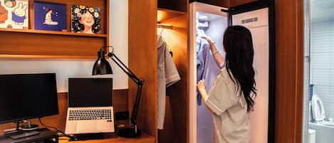 Une chambre d’hôtel équipée d’un bureau, d’un ordinateur, d’une lampe et d’une armoire contenant des vêtements.