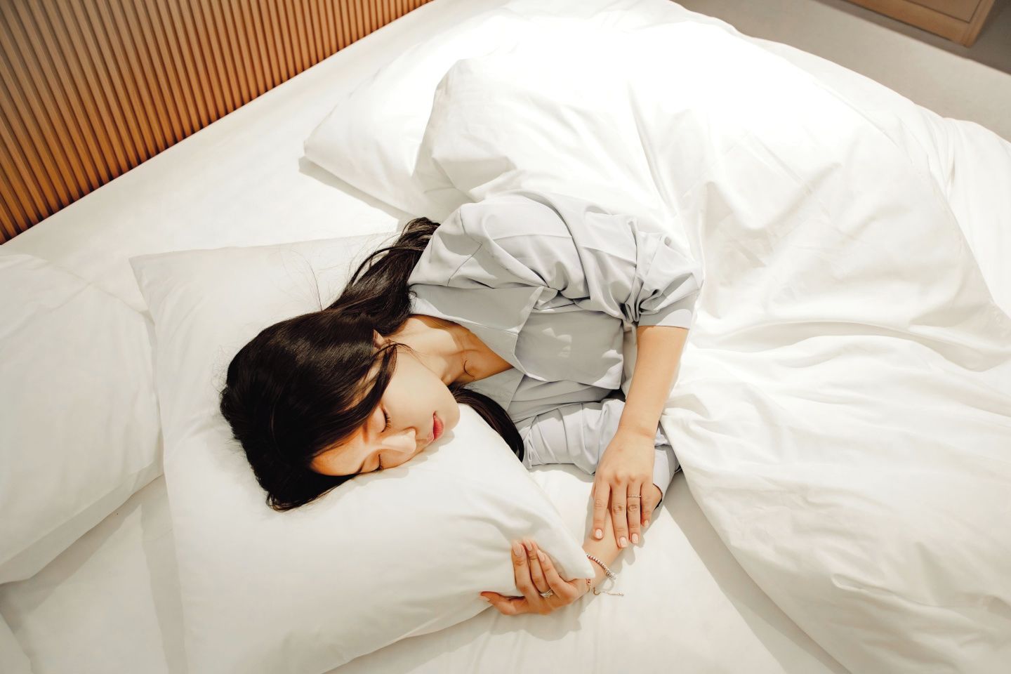 Una persona durmiendo en una cama con ropa de cama blanca.