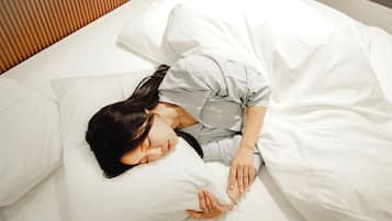 Una persona durmiendo en una cama con ropa de cama blanca.
