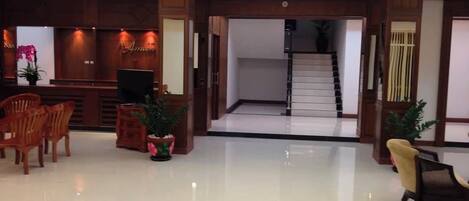 Un área de recepción con mostrador, sillas, plantas en macetas y una escalera que conduce a un piso superior.