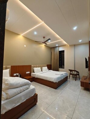 A hotel room with two beds, a ceiling fan, a TV, and a desk. - Sunrise Resorts (jaisalmer)