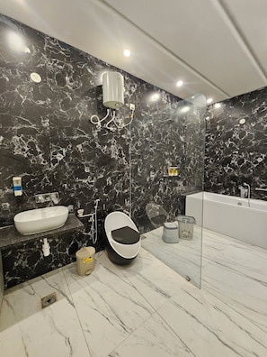 A modern bathroom with a black marble wall, a white sink, a toilet, and a bathtub. - Sunrise Resorts (jaisalmer)