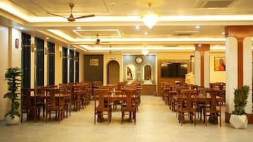 A hotel dining area with multiple wooden tables and chairs, ceiling fans, and a chandelier.