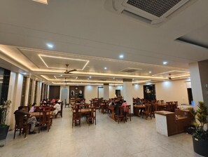 A spacious indoor dining area with multiple tables and chairs, a reception desk, and ceiling fans. - Sunrise Resorts (Jaisalmer)