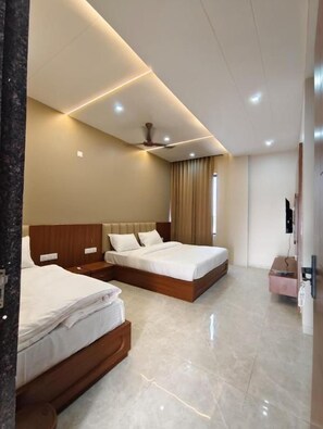 A hotel room with two beds, a ceiling fan, a flat-screen TV, and a minibar. - Sunrise Resorts (jaisalmer)