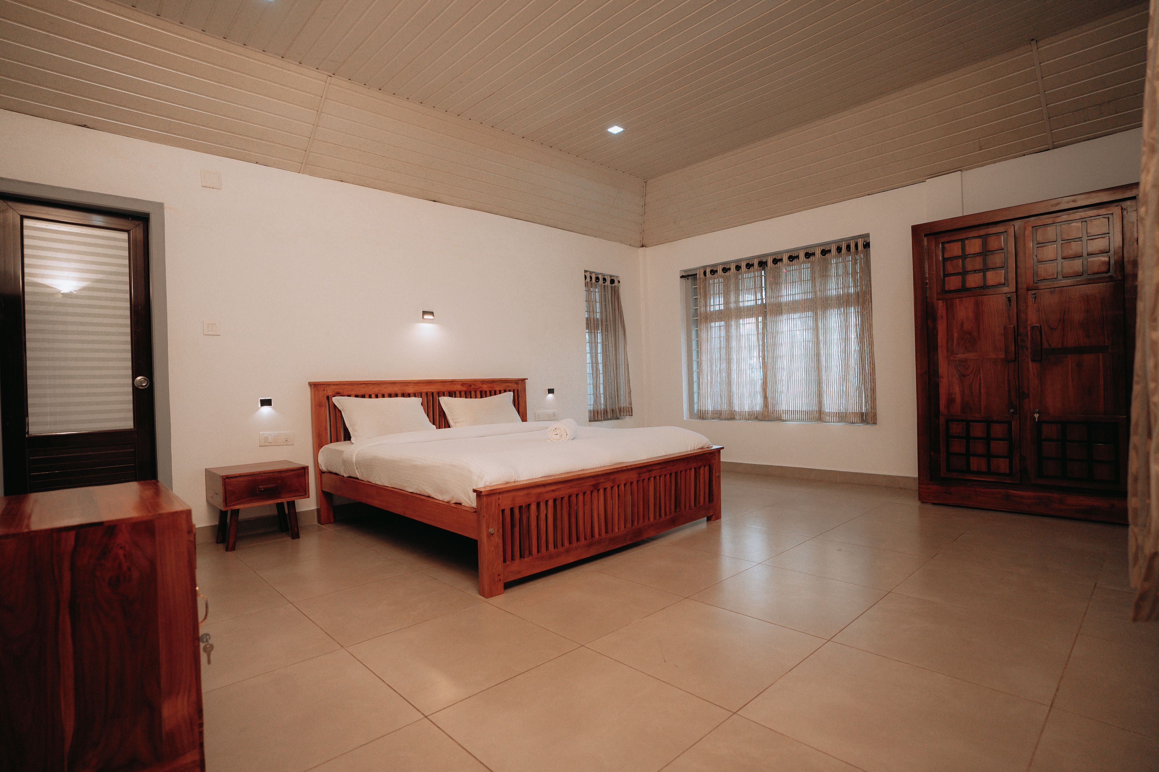 A bedroom with a wooden bed, a nightstand, a wardrobe, and a window with curtains.