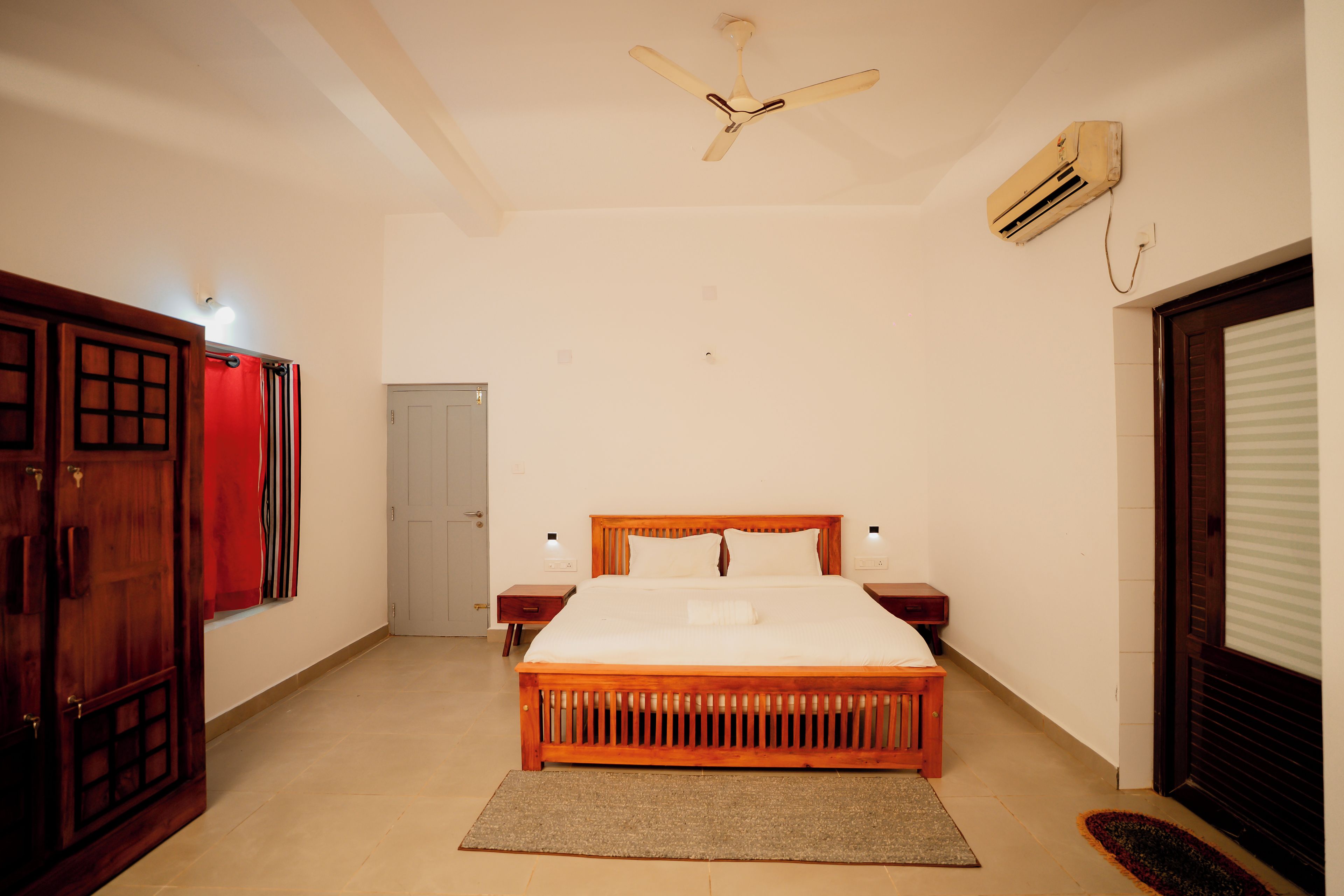 A bedroom with a bed, a ceiling fan, an air conditioning unit, and a door.