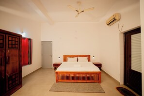Un dormitorio con cama, ventilador de techo, aire acondicionado y una puerta.