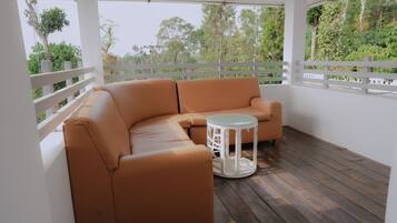 Un sofá seccional color arena y una mesa redonda blanca sobre una terraza de madera con barandillas blancas.