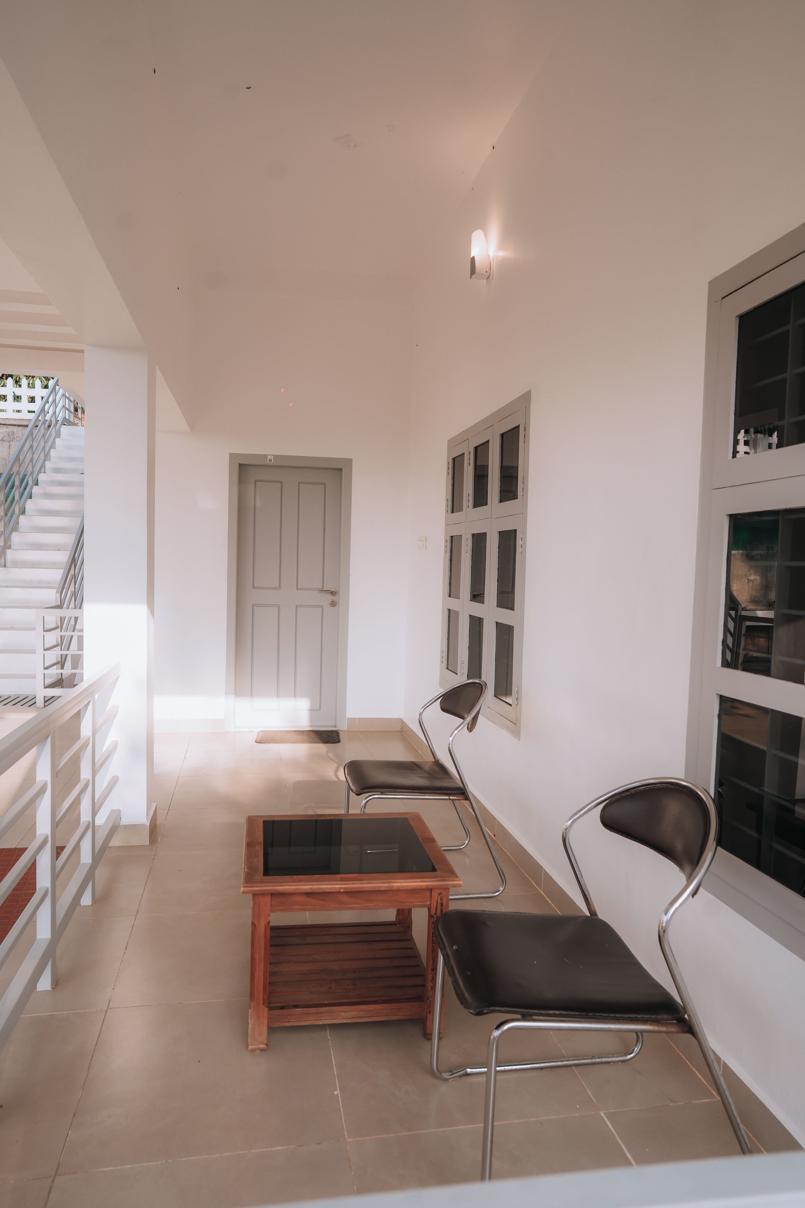 Un interior moderno con una escalera, una puerta y una zona de estar con sillas y una mesa.