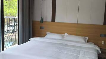 Habitación de hotel con una cama grande, cabecera de madera, vista al exterior desde un balcón y un diseño moderno.