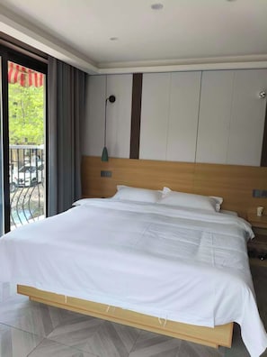 Habitación de hotel con una cama grande, cabecera de madera, vista al exterior desde un balcón y un diseño moderno.