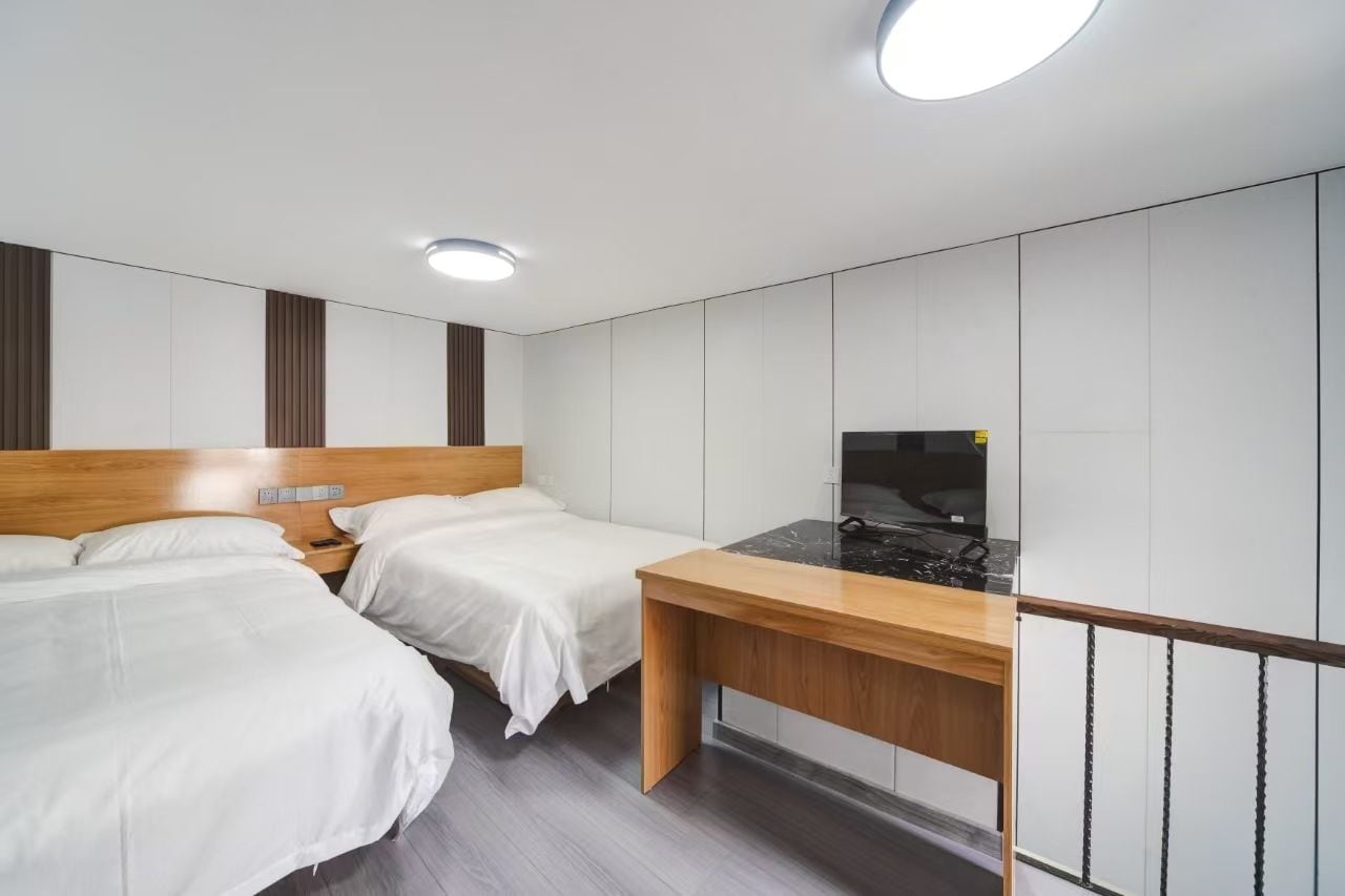 Habitación de hotel moderna con dos camas, un escritorio de madera, un televisor de pantalla plana y armarios empotrados.