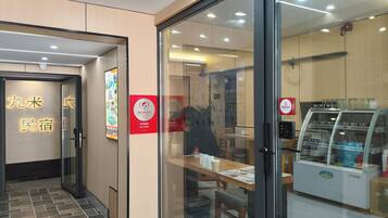 A modern interior with a glass partition, a digital menu board, and a seating area with tables and chairs.