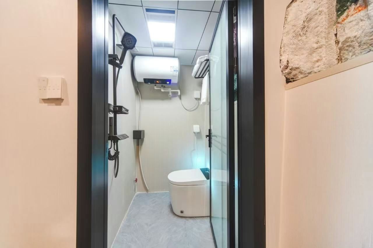 A modern bathroom with a glass partition, a toilet, a shower area, and a wall-mounted air conditioning unit.