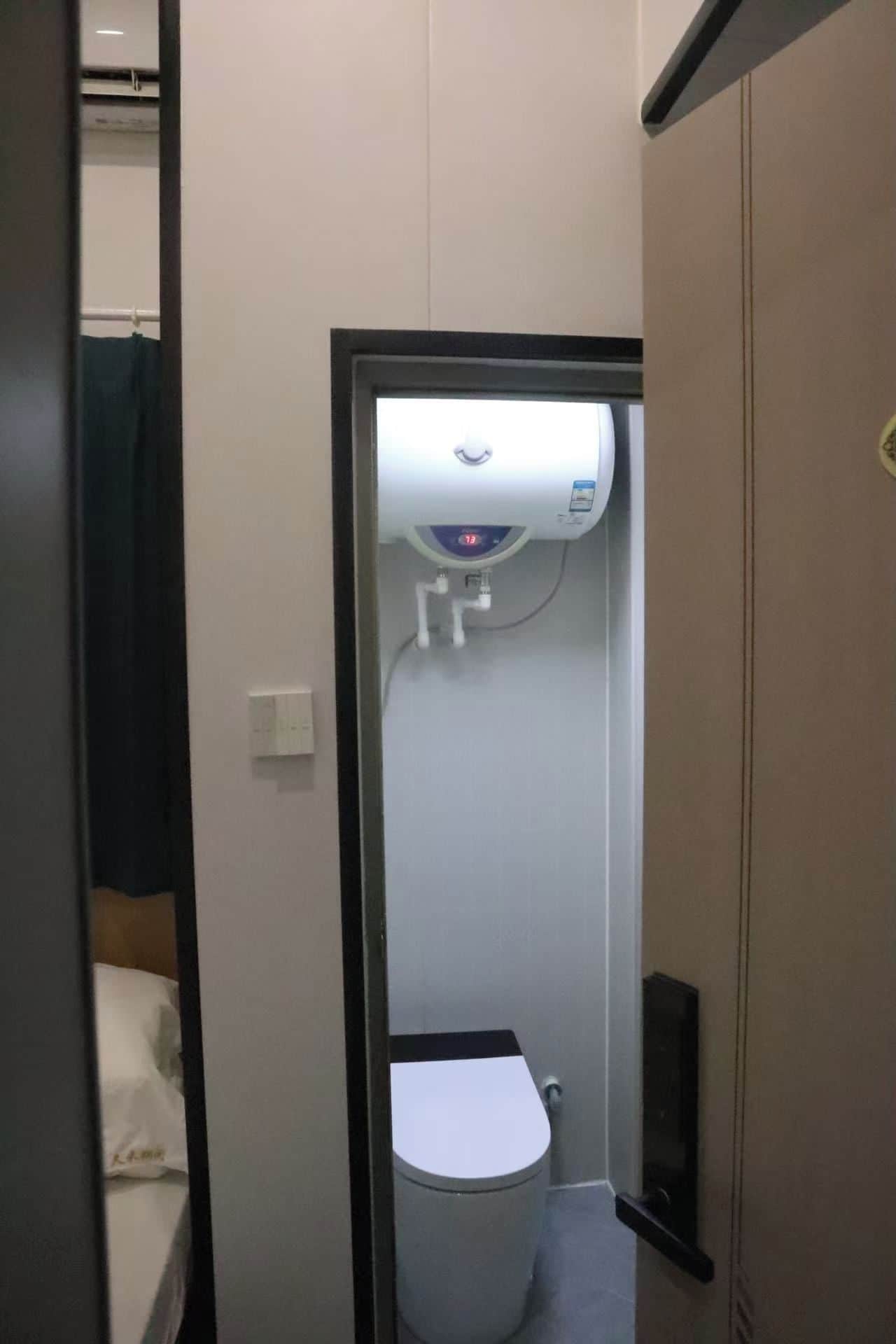 A small, enclosed bathroom with a toilet, a hand dryer, and a water heater.