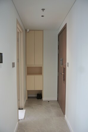 Ein schmaler Gang mit einer Holztür rechts, einem beigefarbenen Schrank mit Ablage in der Mitte und einer weißen Tür links.