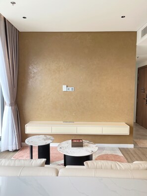 Un salon moderne avec un mur de couleur beige, un canapé, deux tables rondes et un banc intégré.