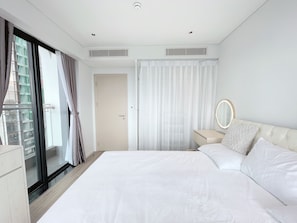 Une chambre moderne avec un grand lit, une table de chevet avec un miroir et une porte-fenêtre coulissante donnant sur un balcon.