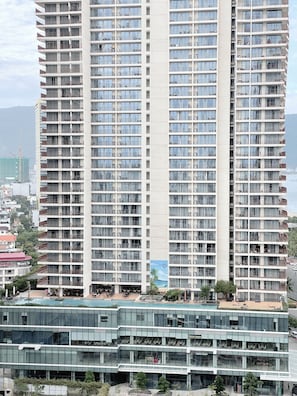 Un immeuble de grande hauteur doté de nombreux balcons, d’un espace piscine sur le toit et d’une façade moderne en verre.