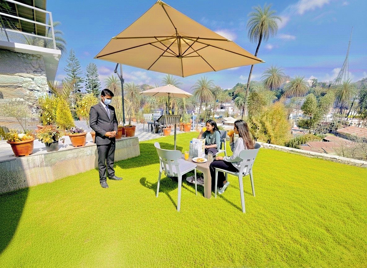 Eine Terrasse mit Tisch und Stühlen, eine stehende Person und ein großer Sonnenschirm.