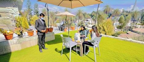 A patio area with a table and chairs, a person standing, and a large umbrella.