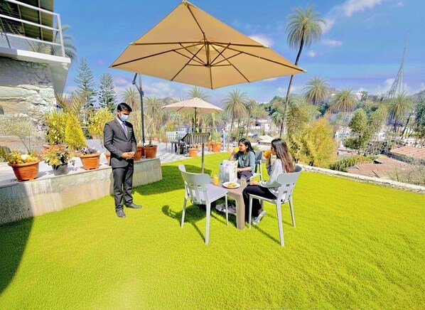 A patio area with a table and chairs, a person standing, and a large umbrella. - Royal Raj Palace Near Nakki Lake Mount Abu (Aburaj)