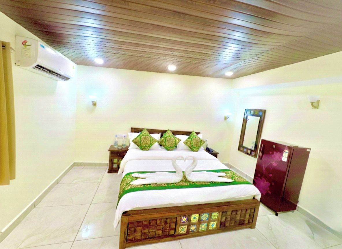 A hotel room with a bed, a nightstand, a mirror, and a refrigerator.