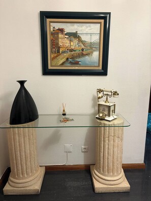 Una taula de consol amb tapa de vidre, amb dues columnes decoratives, un quadre emmarcat a la part superior i un objecte decoratiu petit sobre la taula.