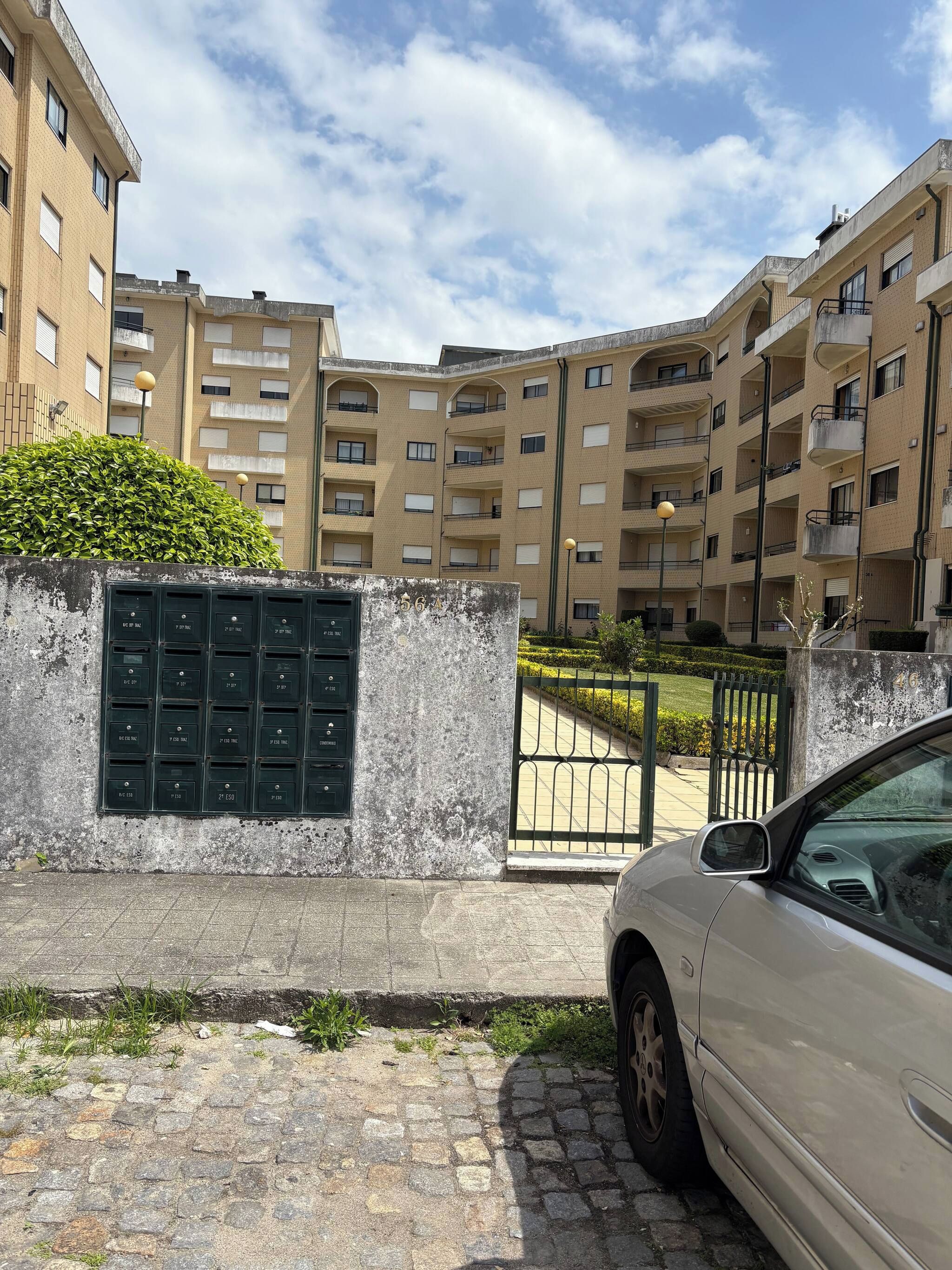 A multi-story residential building with a gated entrance, a mailbox, and a parked car.