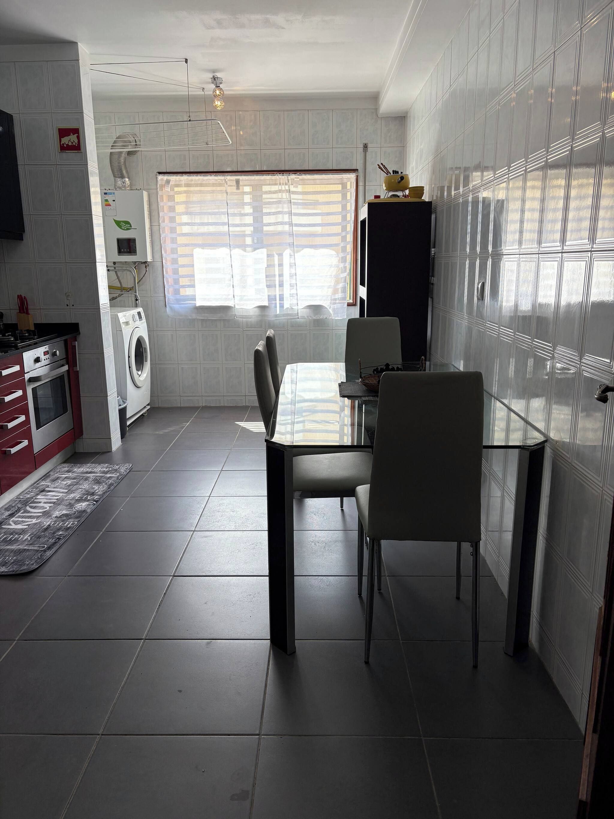 Cocina compacta con lavadora, mesa de comedor y una ventana con persianas.