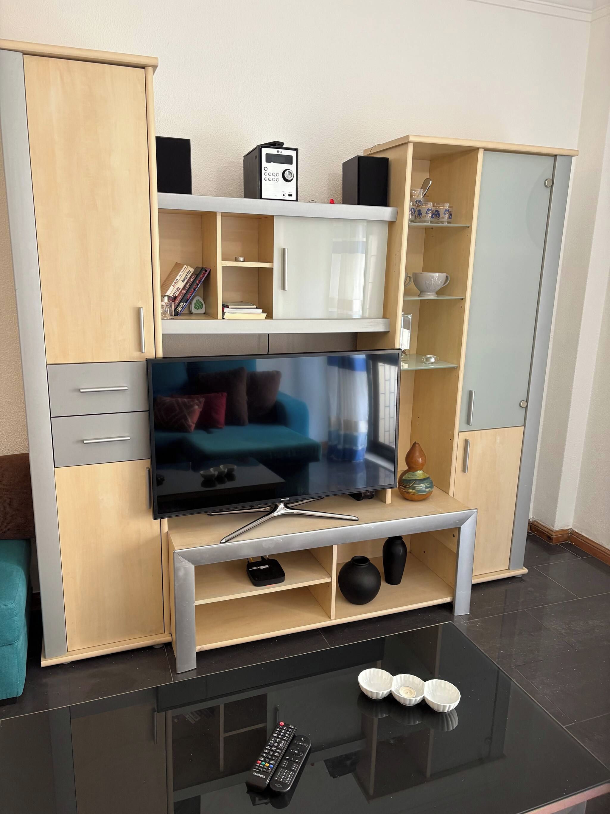 Ein modernes Wohnzimmer mit Flachbildfernseher, Holzschränken und einem Glastisch.